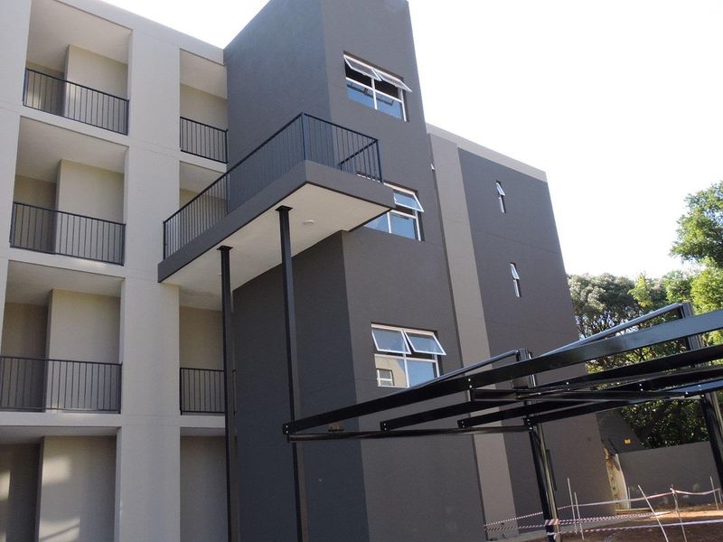 Modern multi-story apartment building exterior featuring clean lines, private balconies with metal railings, and a dedicated carport structure.
