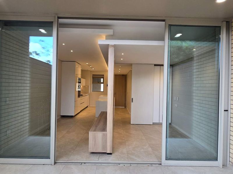 Modern open-plan apartment interior viewed from a patio, featuring sleek cabinetry, recessed lighting, and large sliding glass doors opening to an outdoor space.