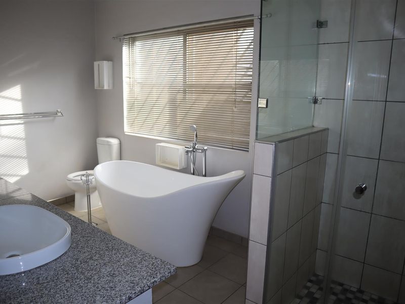 Modern bathroom featuring a freestanding bathtub, glass-enclosed shower, granite vanity with vessel sink, and neutral tiled finishes.