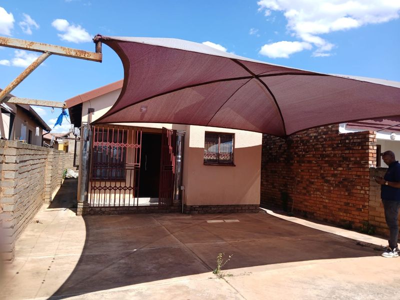 Front exterior view of the property featuring a concrete driveway, a large shade sail, and secure metal gate access.