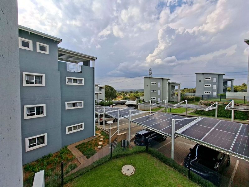 Exterior view of an apartment complex featuring modern multi-story buildings, landscaped grounds, and covered parking bays equipped with solar panels.