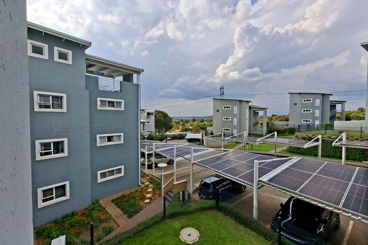 Exterior view of an apartment complex featuring modern multi-story buildings, landscaped grounds, and covered parking bays equipped with solar panels.