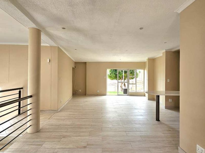 Spacious open-plan living area featuring neutral tiled flooring, recessed lighting, and a structural column, leading out to a rear garden through sliding glass doors.