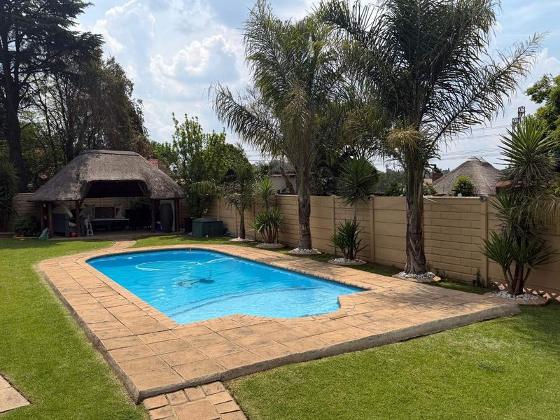 A well-maintained outdoor area featuring a swimming pool, paved surround, and a thatched lapa, enclosed by a secure precast concrete boundary wall.