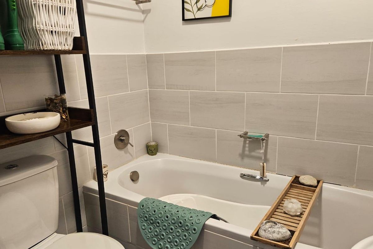 A clean, modern bathroom featuring a white bathtub with neutral subway-style wall tiling and chrome fixtures.