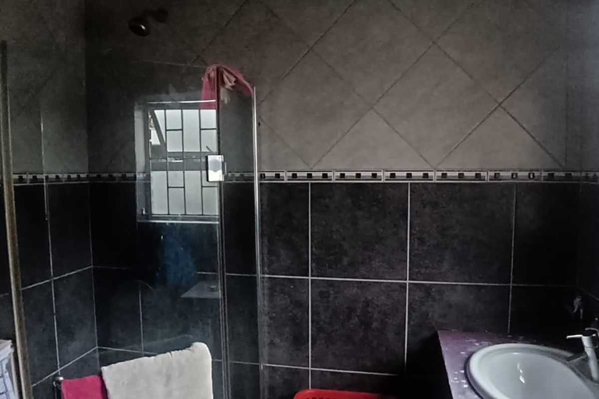 A bathroom featuring a shower enclosure, vanity basin, and dark tiled walls with security bars on the window.