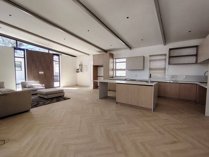 Spacious open-plan living and kitchen area featuring modern light wood cabinetry, a central island, herringbone flooring, and high ceilings with exposed beams.