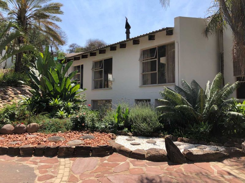 Rear view of the property featuring a white facade with exposed timber rafters, casement windows, and a well-maintained landscaped garden with stone paving.