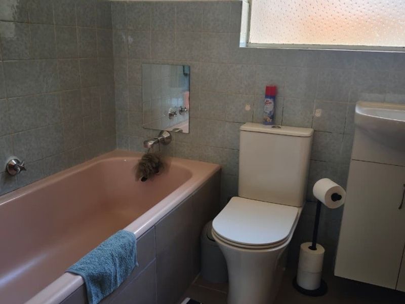 A compact bathroom featuring a vintage pink bathtub, a white toilet, and a vanity cabinet with a basin, finished with wall tiling.