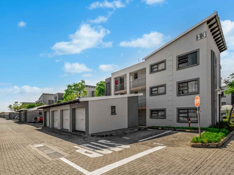 Exterior view of a modern apartment complex featuring paved driveway access, multiple lock-up garages, and secure balcony access for residents.