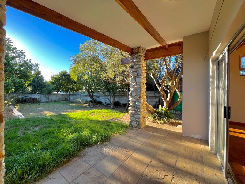 Covered patio featuring a rustic stone-clad pillar and exposed timber beams, overlooking a private garden with established trees and a concrete boundary wall.
