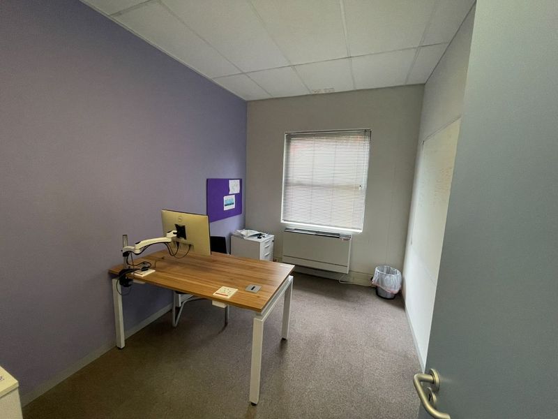 A functional office space featuring a suspended ceiling, wall-mounted heater, and a whiteboard, providing a practical environment for professional work.