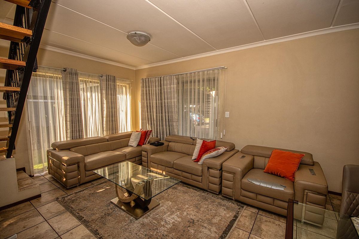 A spacious living room featuring tiled flooring, large windows with natural light, and an integrated staircase leading to the upper level.