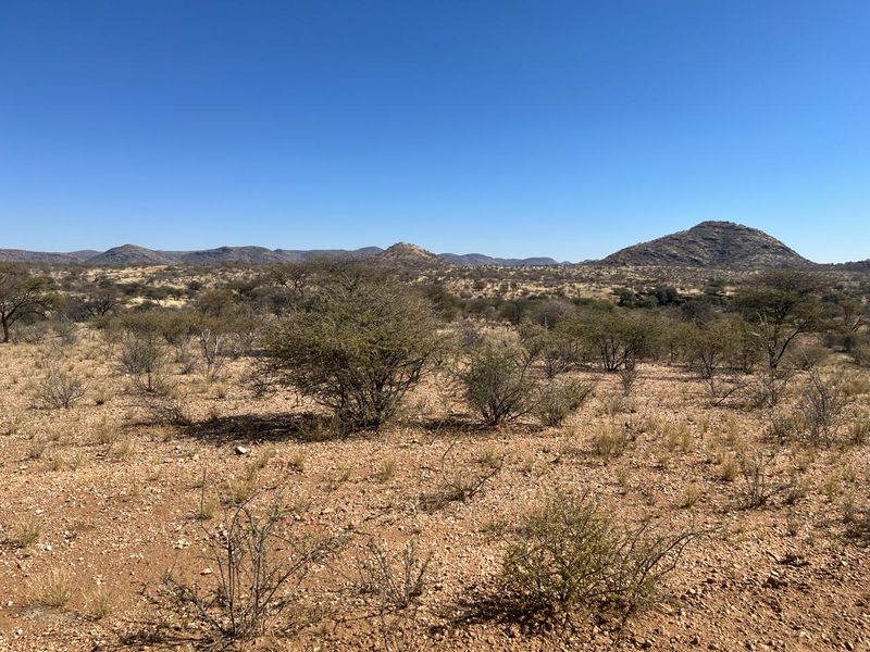 A scenic view of the natural landscape featuring arid terrain, native shrubs, and distant mountain ranges under a clear blue sky.