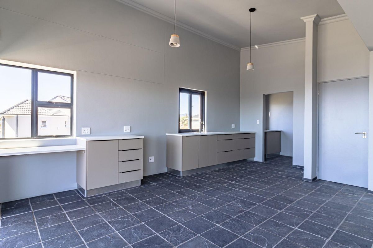 A modern, spacious kitchen area featuring sleek cabinetry, stone countertops, dark tiled flooring, and pendant lighting, with an adjacent scullery area.
