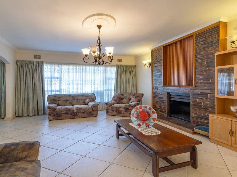 Spacious living room featuring a prominent stone-clad fireplace, ceramic tiled flooring, and classic ceiling detailing, offering a comfortable and traditional living space.