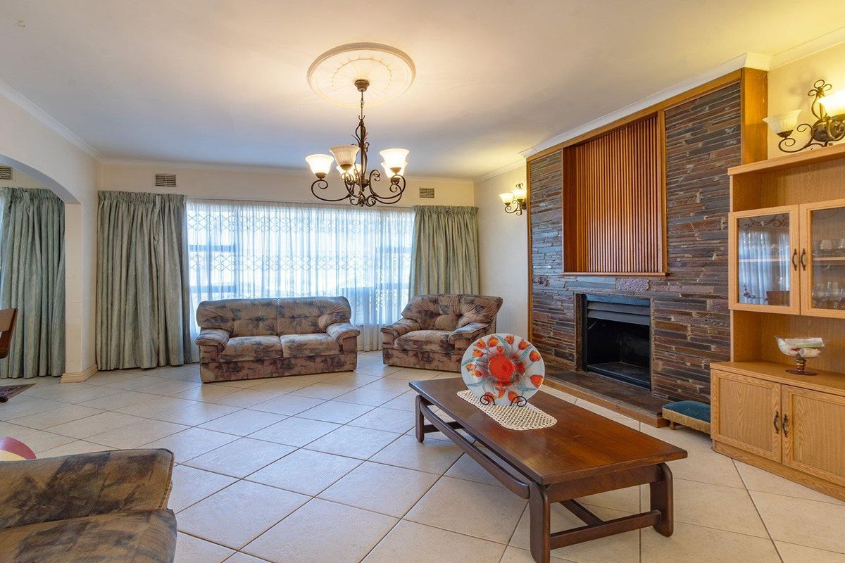 Spacious living room featuring a prominent stone-clad fireplace, ceramic tiled flooring, and classic ceiling detailing, offering a comfortable and traditional living space.
