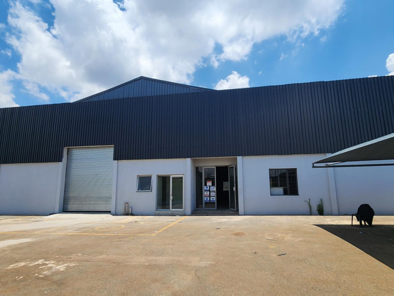 Front elevation of an industrial warehouse featuring a large roller shutter door, paved forecourt, and a shade cloth carport structure.