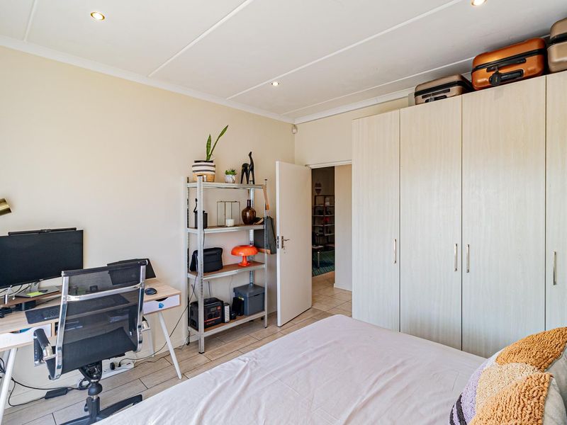 A functional bedroom featuring light-toned built-in wardrobes, tiled flooring, and recessed ceiling lighting, providing a clean and practical living space.