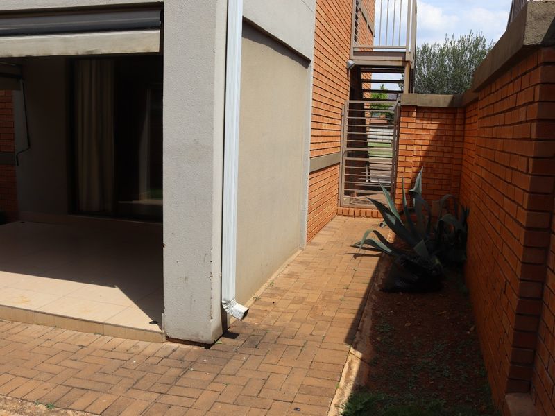 Rear exterior view of the apartment featuring a paved patio area, brick boundary wall, and an external metal staircase.