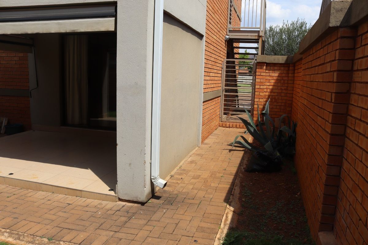 Rear exterior view of the apartment featuring a paved patio area, brick boundary wall, and an external metal staircase.