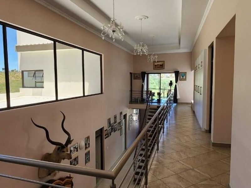 Spacious upper-level hallway featuring tiled flooring, a metal balustrade overlooking the lower level, recessed ceiling details, and built-in storage cupboards.