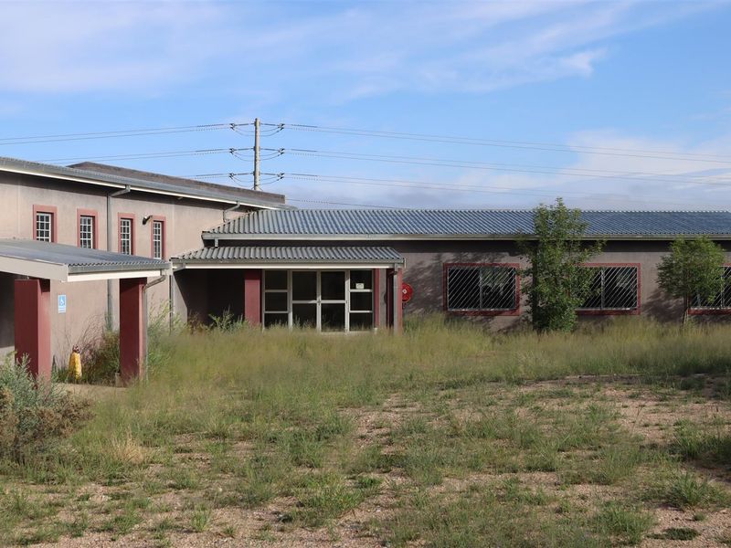 Front exterior view of a single-story commercial or mixed-use building featuring a metal roof, security bars, and an overgrown yard area.