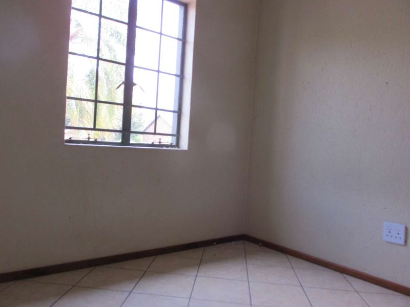 A vacant bedroom featuring tiled flooring, neutral walls, and a window fitted with security burglar bars.