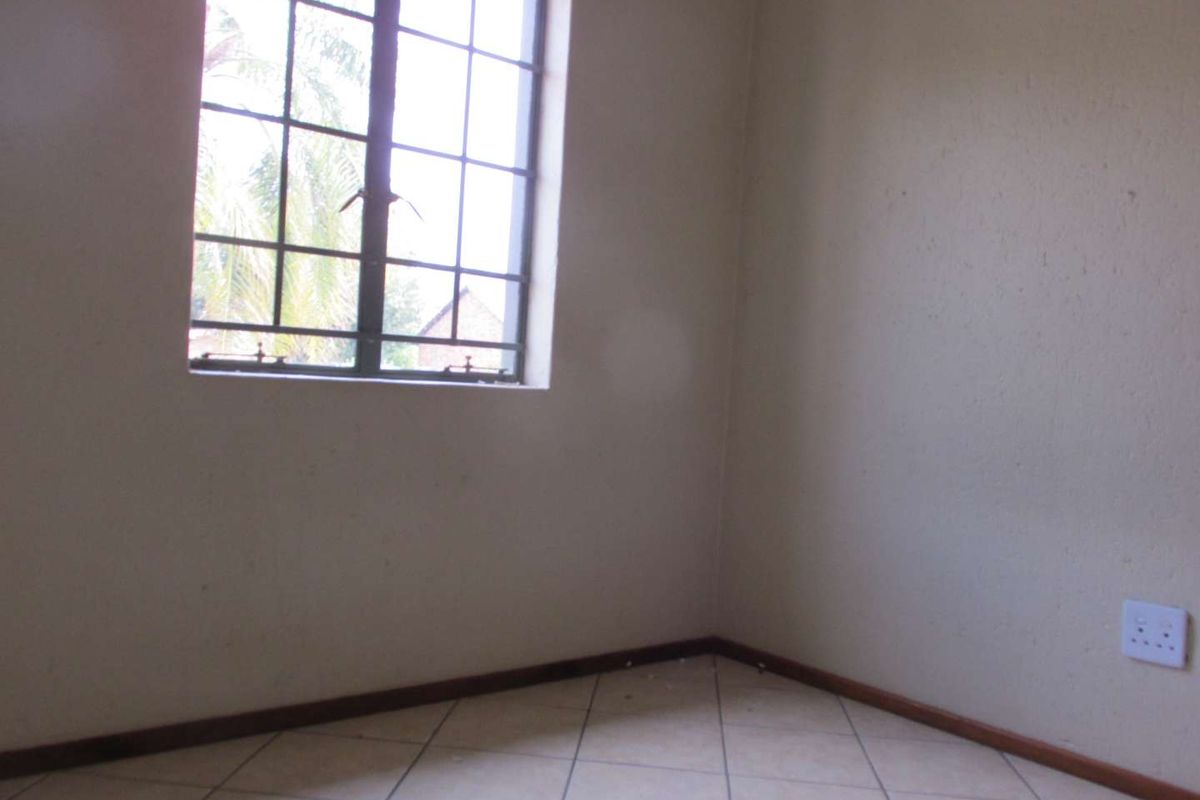 A vacant bedroom featuring tiled flooring, neutral walls, and a window fitted with security burglar bars.