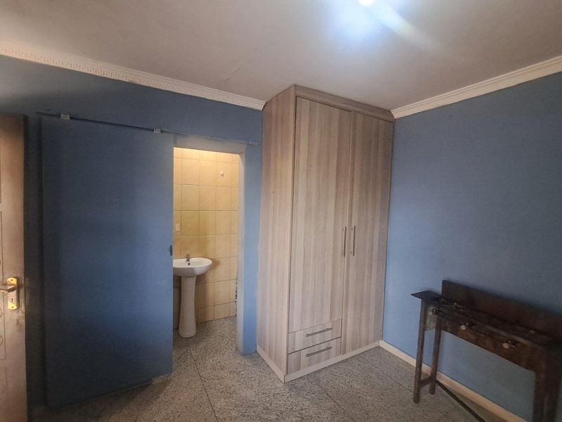 Bedroom featuring a built-in wardrobe, tiled flooring, and an en-suite bathroom area with a pedestal basin.