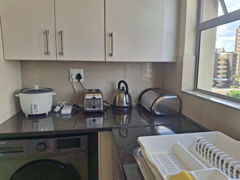A functional kitchen area featuring granite countertops, built-in cabinetry, and an integrated washing machine, providing a practical and efficient workspace.