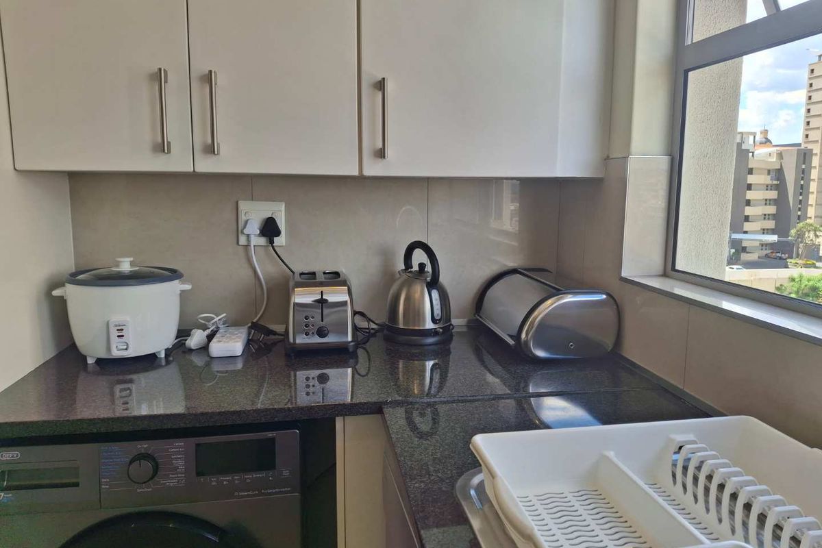 A functional kitchen area featuring granite countertops, built-in cabinetry, and an integrated washing machine, providing a practical and efficient workspace.