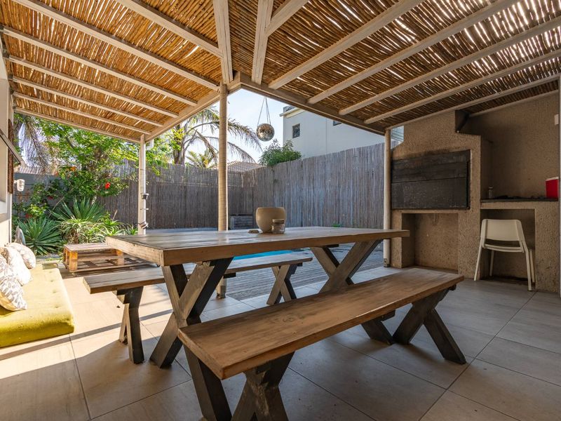Covered outdoor patio featuring a thatched roof, tiled flooring, and a built-in braai area, perfect for alfresco dining and entertaining.