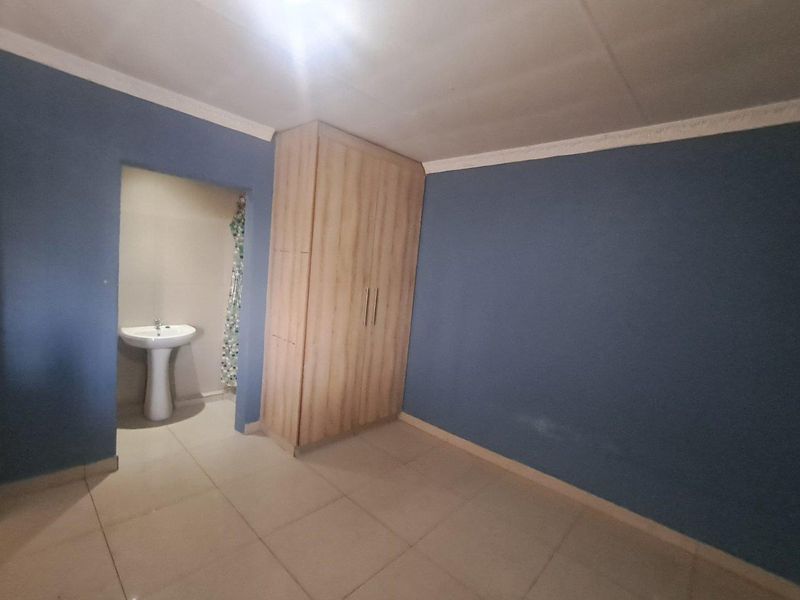 A bedroom featuring tiled flooring, a built-in wardrobe, and an adjoining alcove with a pedestal basin.