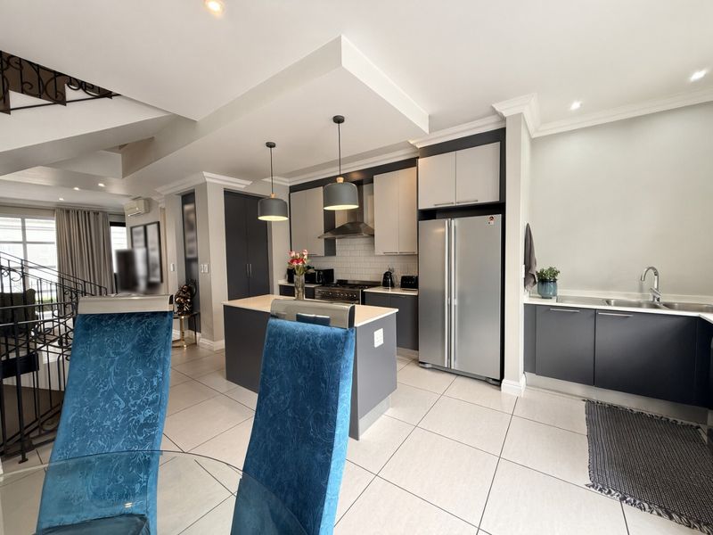 Modern open-plan kitchen featuring dark cabinetry, a central island, stainless steel appliances, tiled flooring, and recessed lighting, seamlessly integrated into the living space.