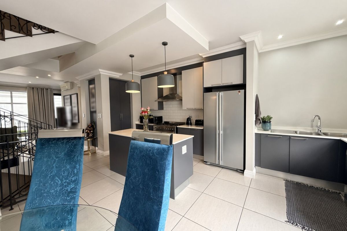 Modern open-plan kitchen featuring dark cabinetry, a central island, stainless steel appliances, tiled flooring, and recessed lighting, seamlessly integrated into the living space.