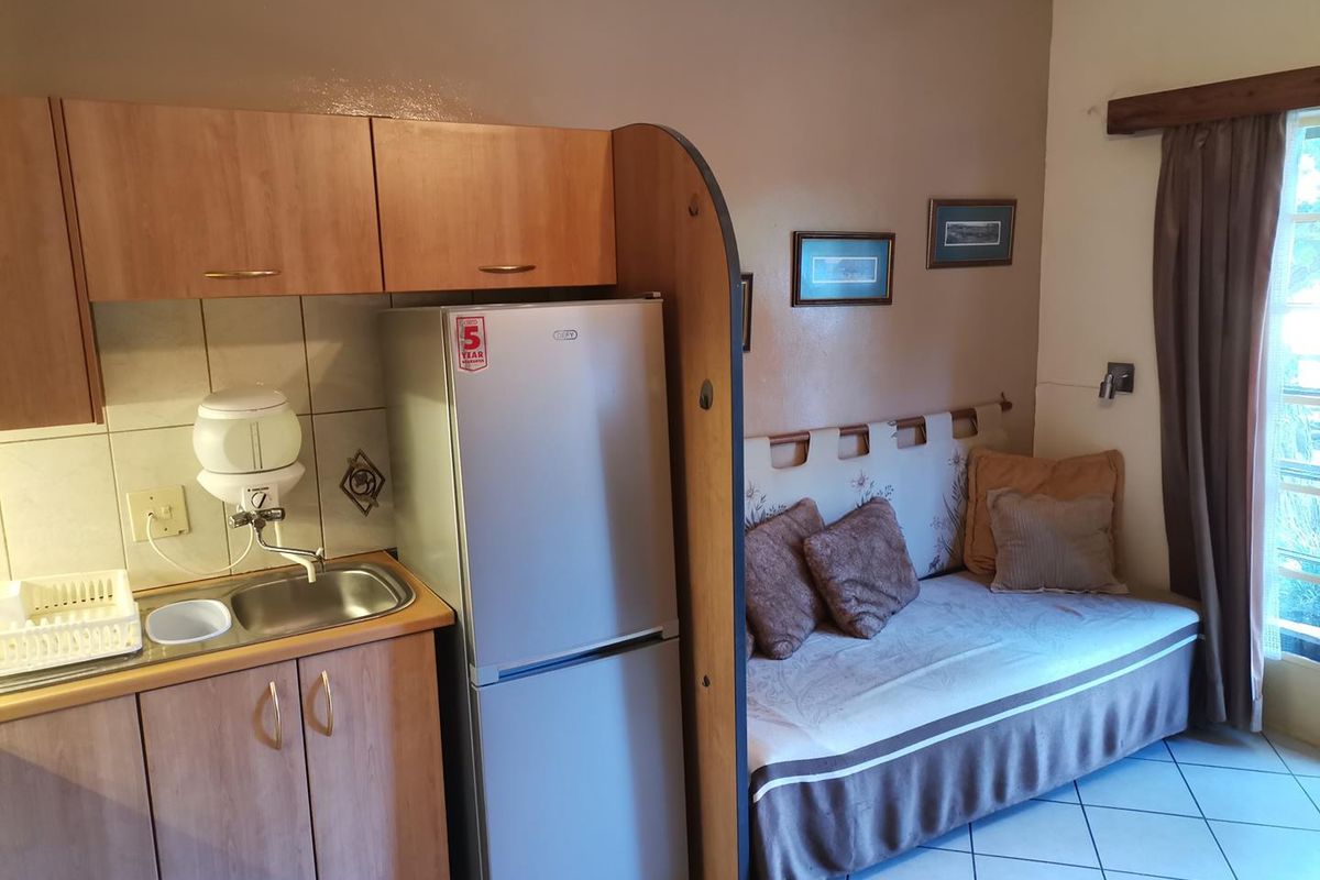 Compact open-plan studio apartment featuring a kitchenette with built-in cabinetry, stainless steel sink, and tiled flooring with direct access to natural light.