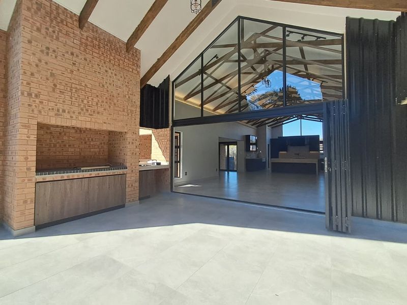 Spacious covered patio featuring a built-in braai, exposed timber trusses, and large bi-fold doors opening into an expansive open-plan living area.