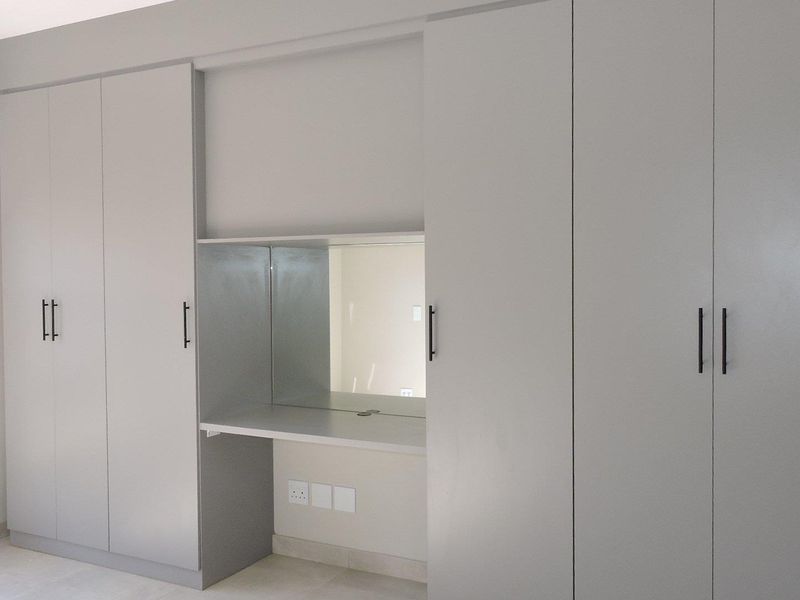 A bright bedroom featuring modern, floor-to-ceiling built-in cupboards with an integrated vanity desk and mirror.