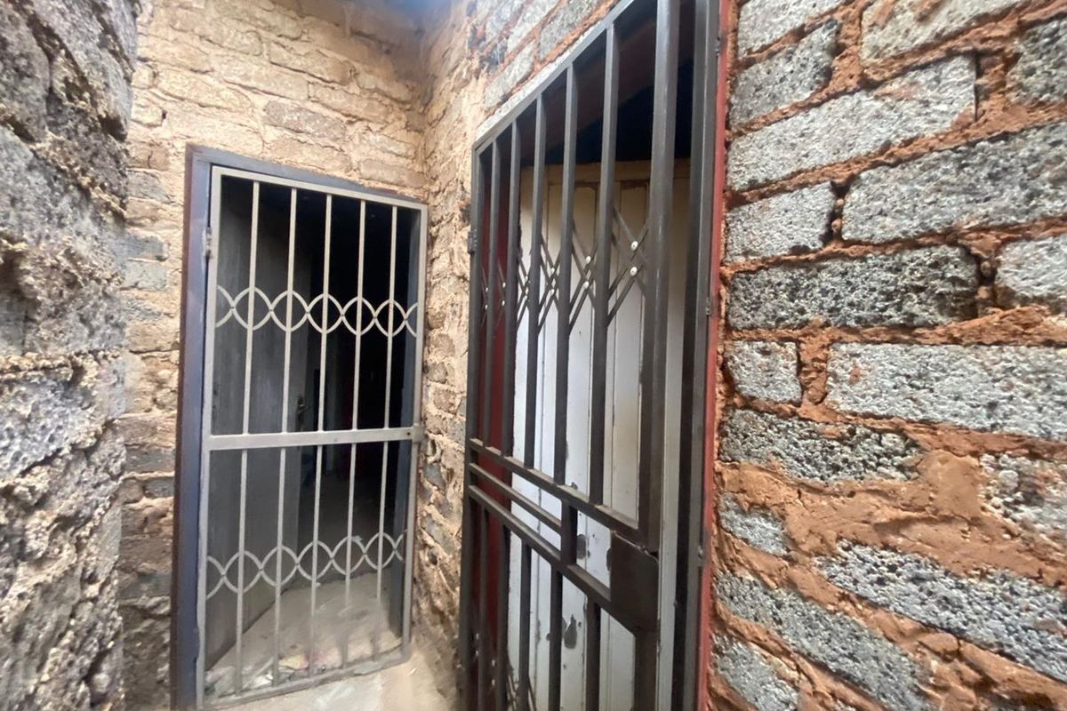 A narrow exterior passage featuring exposed brick walls and metal security gates over doorways.