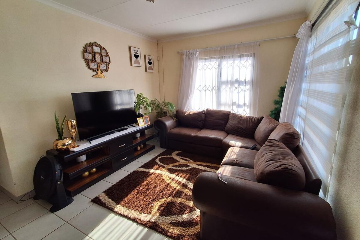 A comfortable living room featuring tiled flooring, large windows with security gates, and neutral wall finishes, providing a functional space for relaxation.