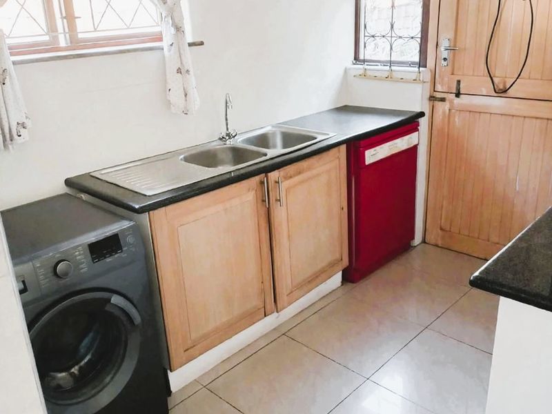 Functional scullery area featuring tiled flooring, double sink with mixer tap, laminate cabinetry, and direct access to the exterior via a timber door.