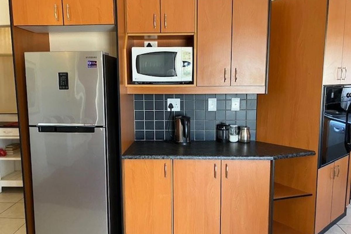 A functional kitchen featuring wood-look laminate cabinetry, dark tiled backsplash, and integrated appliance housing for a microwave and oven.