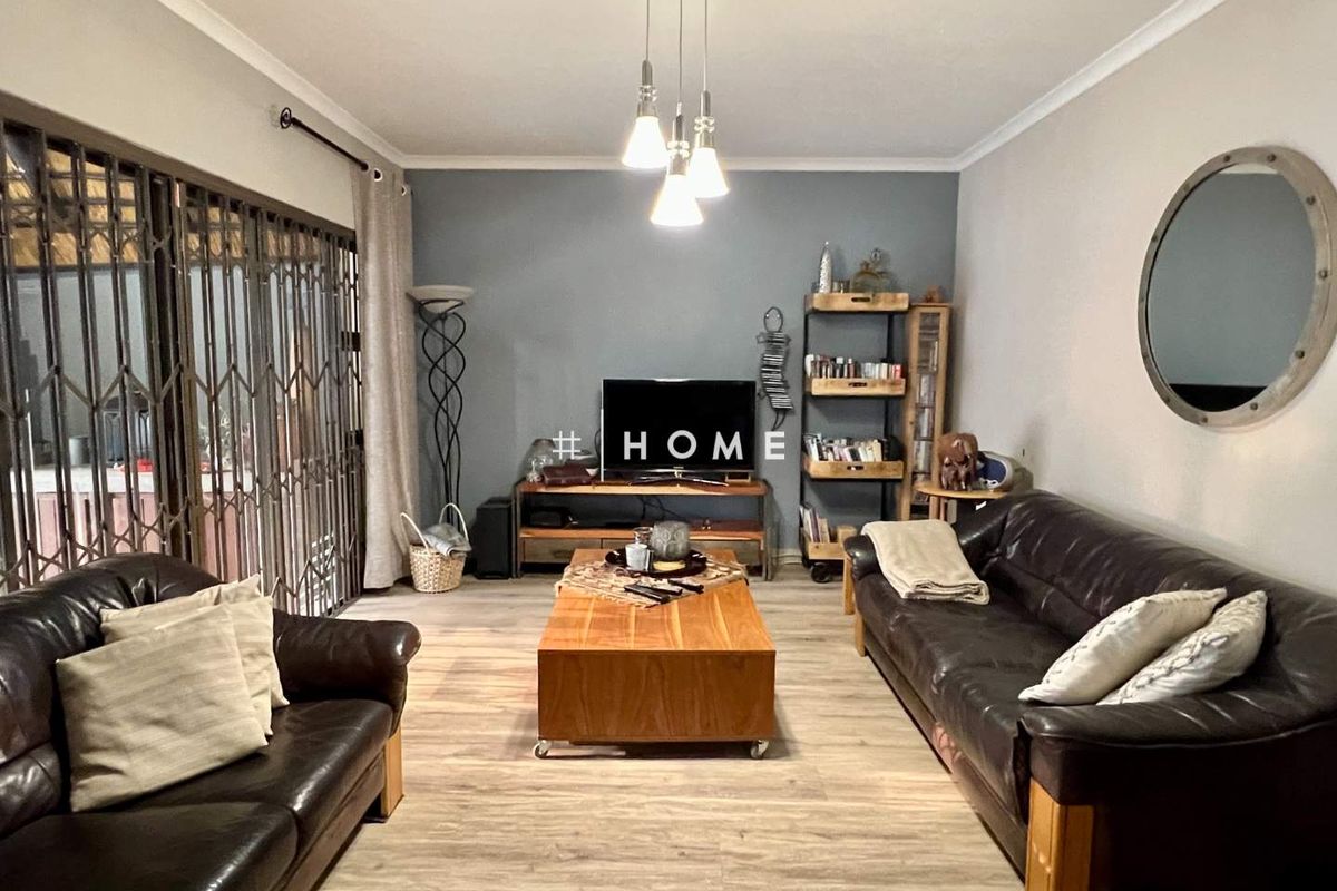A comfortable living room featuring light wood-look flooring, a feature accent wall, and sliding security gates leading to an outdoor area.
