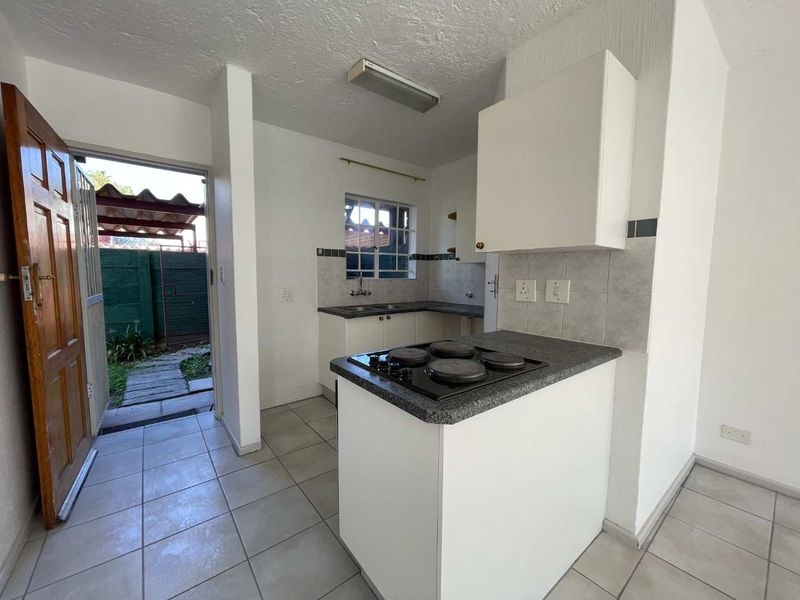 A functional kitchen featuring built-in cabinetry, an electric hob, tiled splashbacks, and direct access to the exterior garden area.