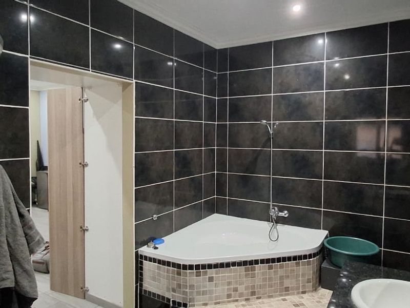 A bathroom featuring dark wall tiles, a corner bathtub with mosaic detailing, a separate shower enclosure, and a vanity basin.
