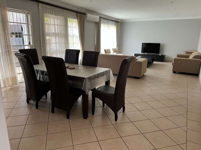 Spacious open-plan living and dining area featuring neutral tiled flooring, recessed lighting, and large sliding doors providing ample natural light.