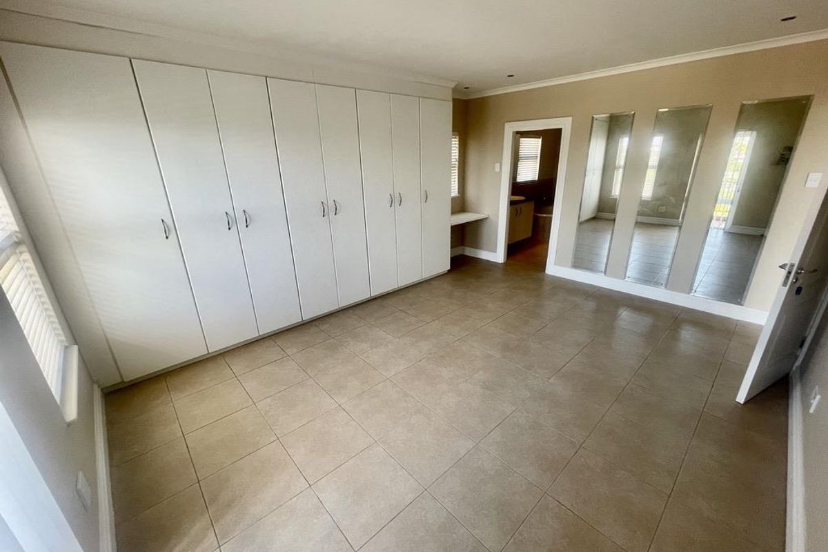 A spacious bedroom featuring extensive built-in cabinetry, tiled flooring, and mirrored wall panels, with an adjoining en-suite bathroom visible through the doorway.