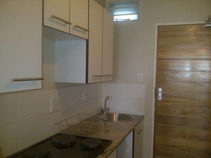 Compact kitchen featuring built-in cabinetry, granite countertops, a stainless steel sink, and an electric hob with tiled splashback.