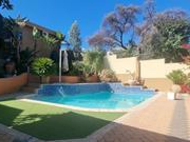 A well-maintained outdoor pool area featuring a paved patio, artificial grass section, and surrounding boundary walls, ideal for relaxation and outdoor entertainment.